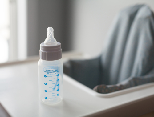 A bottle sitting on the table of a baby chair.