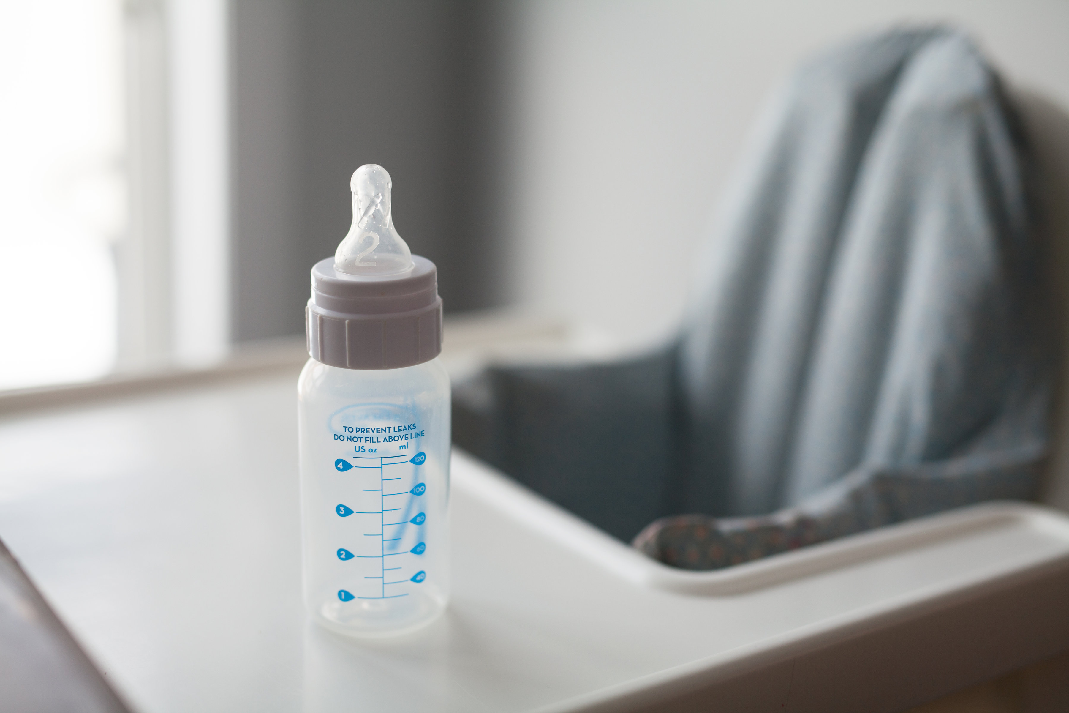 A bottle sitting on the table of a baby chair.