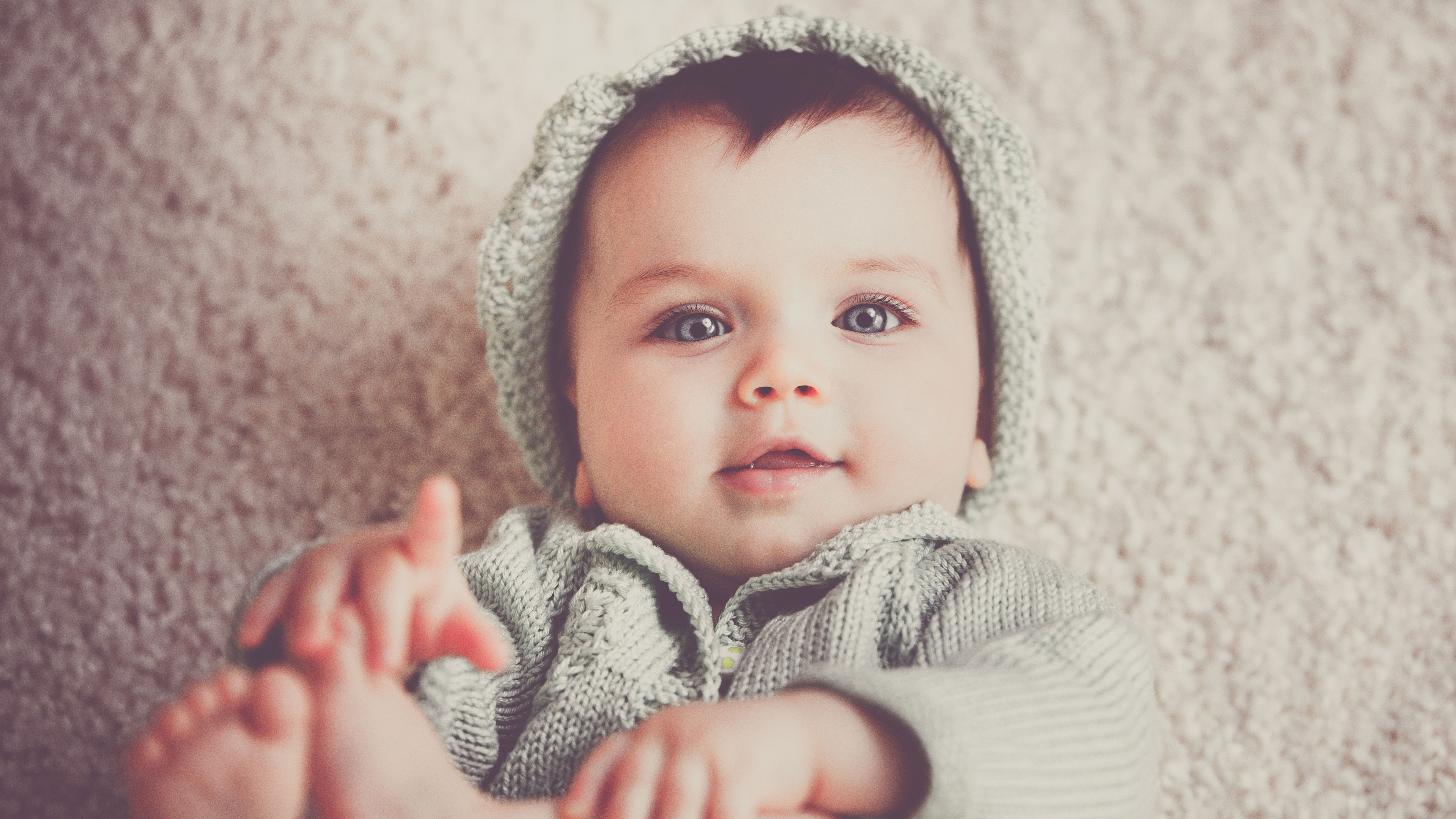 Baby playing with feet while looking forward wearing a hat.