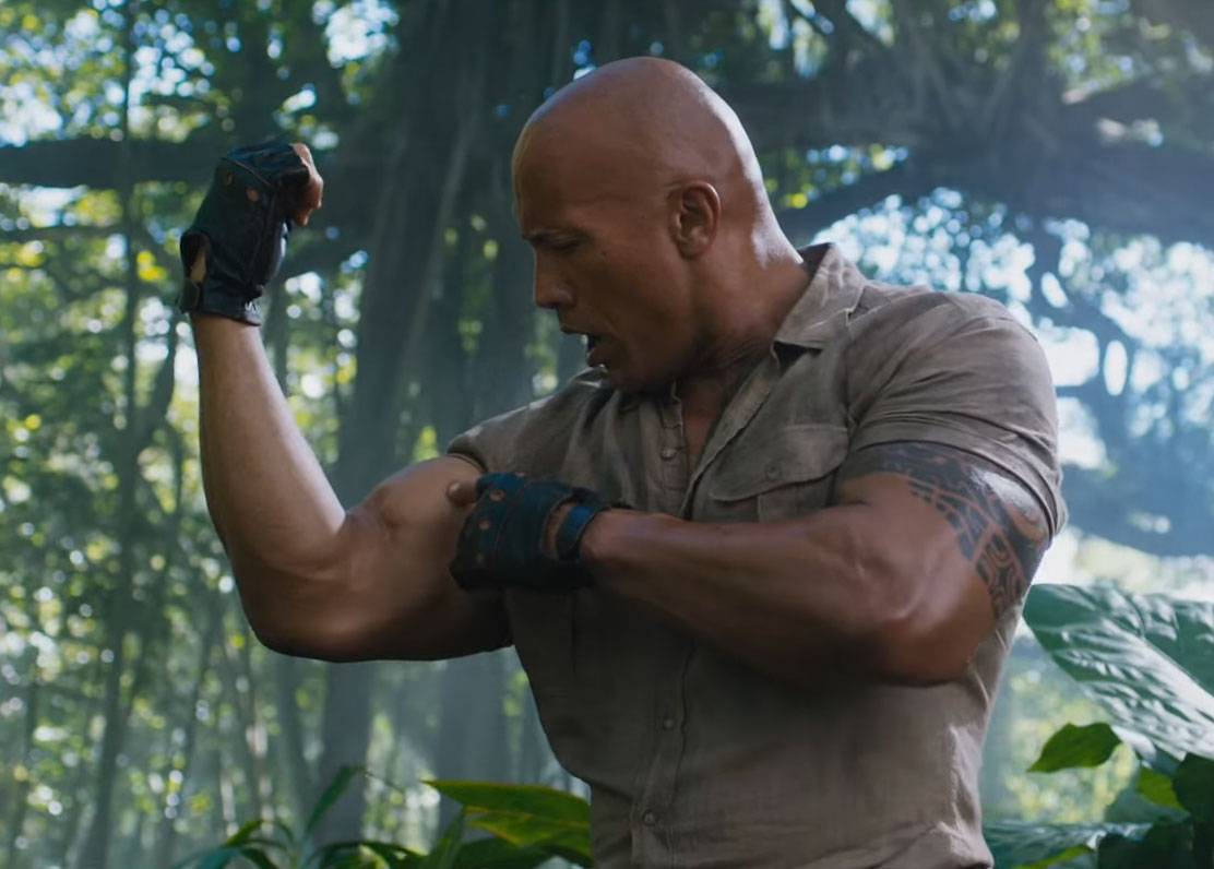The Rock checks out his own muscles in Jumanji: Welcome To The Jungle.