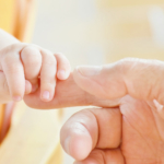 A baby's hand gripping an adult finger,