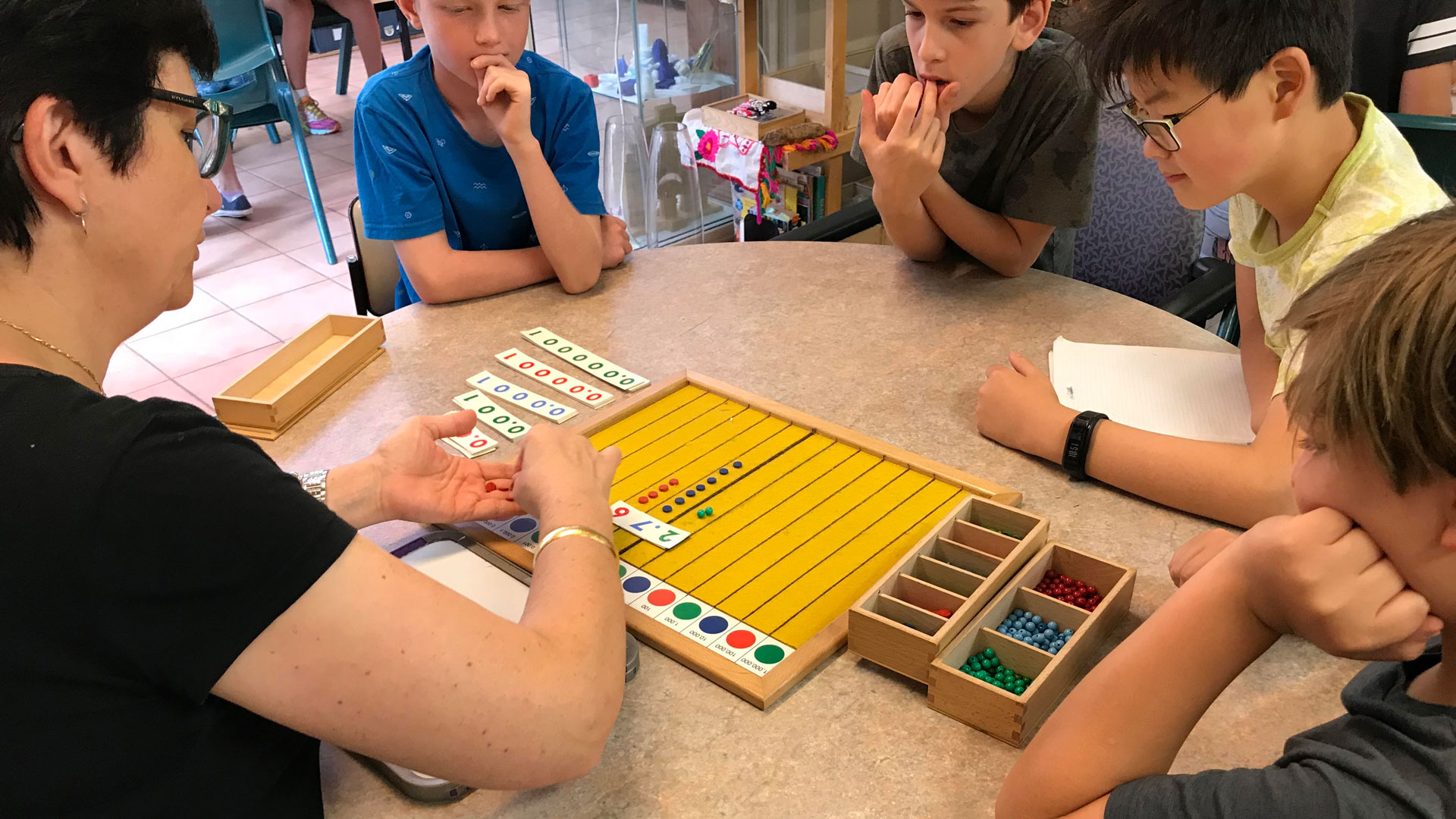 A Montessori teacher explains a maths exercise to students
