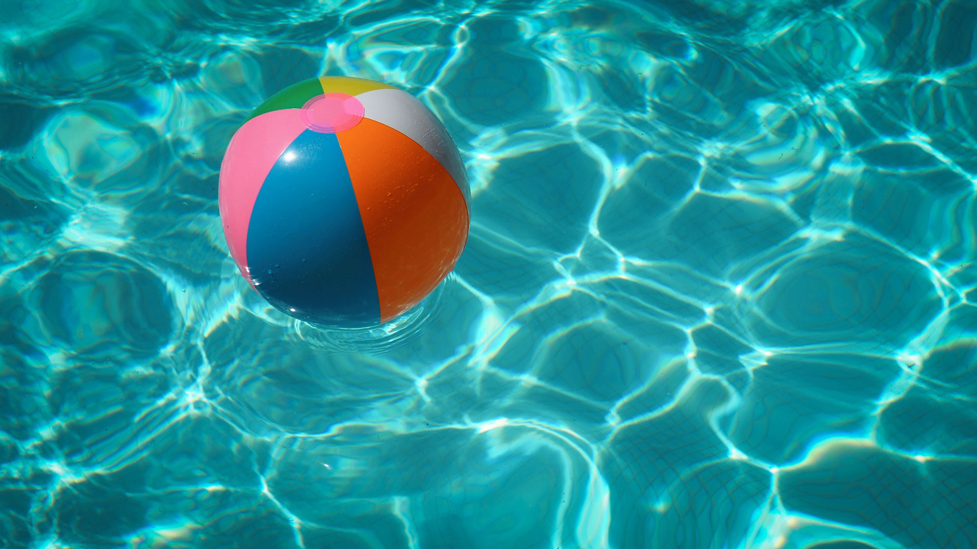 A rainbow beachball floating in a blue swimming pool.